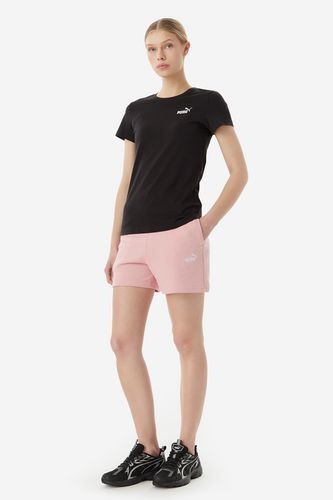 Modelka w T-shircie i szortach, ujęcie całej sylwetki stojącej.