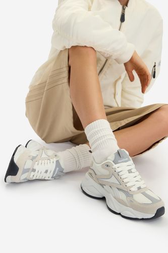 Modelka siedząca, na stopach buty sportowe widziane pod kątem z boku.