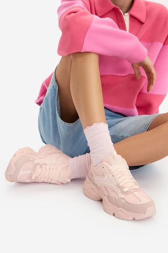 Modelka siedząca, prezentująca buty sportowe na stopach.