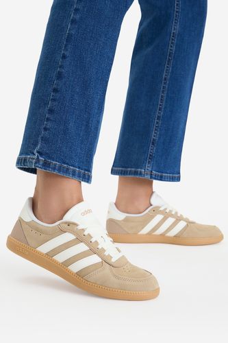 Modelka w spodniach prezentująca buty sportowe na stopach, ujęcie z boku.