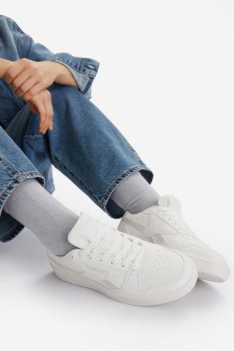 Modelka siedząca, prezentująca buty sportowe na stopach.