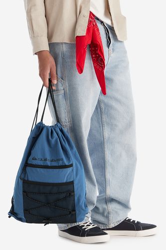 Model trzymający plecak worek w dłoni, sznurki zwisające w dół.