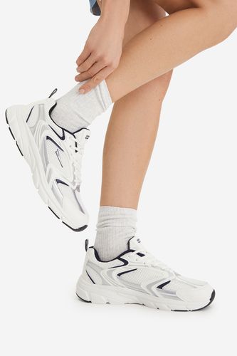 Modelka prezentująca buty sportowe na stopach, nogi skrzyżowane w kolanach.