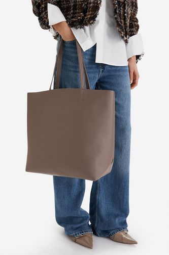 Modelka prezentująca torebkę shopper trzymaną w dłoni u dołu kadru.