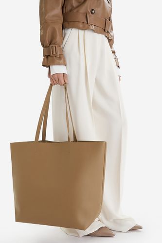 Modelka trzymająca dużą torebkę shopper w dłoni, ujęcie sylwetki od pasa w dół.
