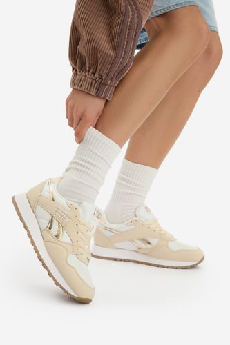 Modelka pochylona, prezentująca buty na stopach, ujęcie nóg od góry.