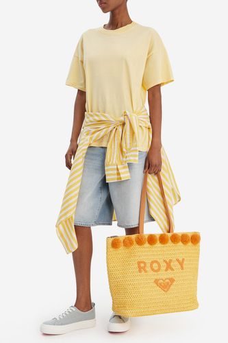 Modelka stojąca, trzymająca dużą torebkę shopper opuszczoną w dół.
