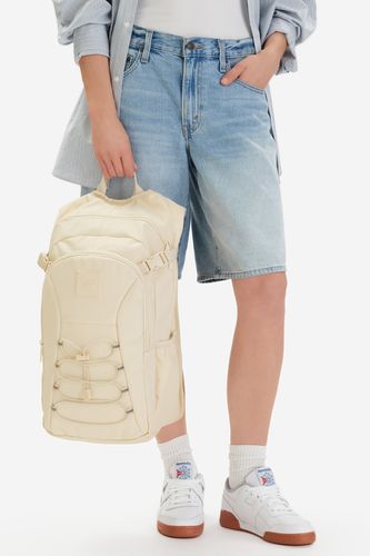 Modelka stojąca, trzymająca plecak za górną rączkę.