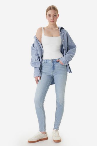 Modelka w spodniach jeansowych i rozpiętej koszuli, ujęcie sylwetki od przodu.