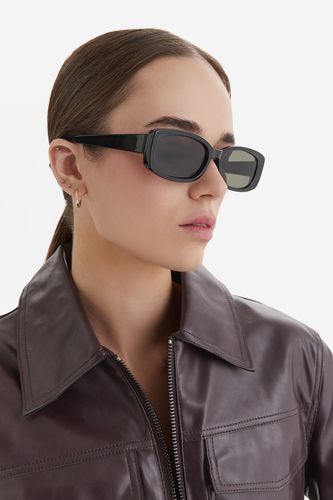 Modelka w kurtce, prezentująca okulary przeciwsłoneczne.