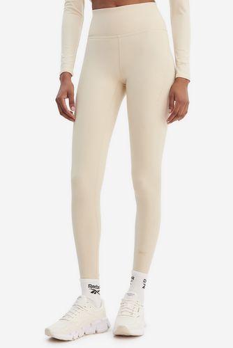 Modelka w legginsach sportowych, frontalny kadr od pasa w dół.