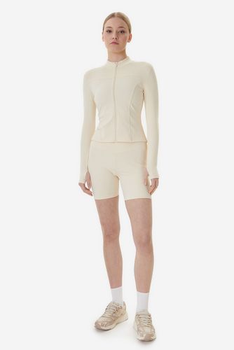 Modelka w bluzie i szortach, pełna sylwetka w sportowym obuwiu.
