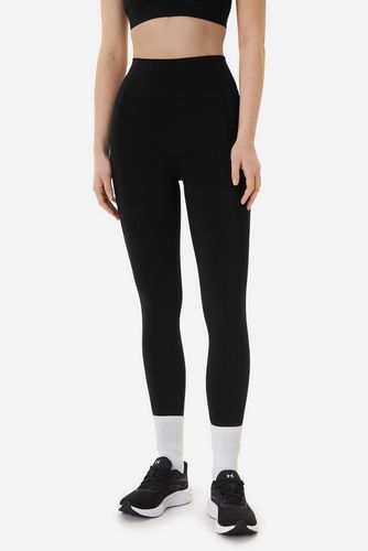 Modelka prezentująca legginsy sportowe, ujęcie sylwetki od przodu od pasa w dół.