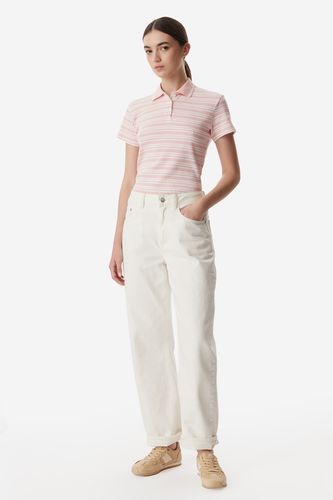 Modelka w koszulce polo i spodniach, pełna sylwetka widziana z przodu.