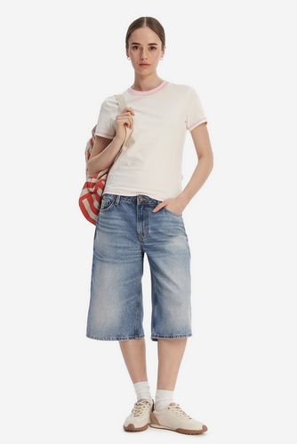 Modelka w T-shircie i dżinsowych spodenkach, sylwetka widoczna z przodu.